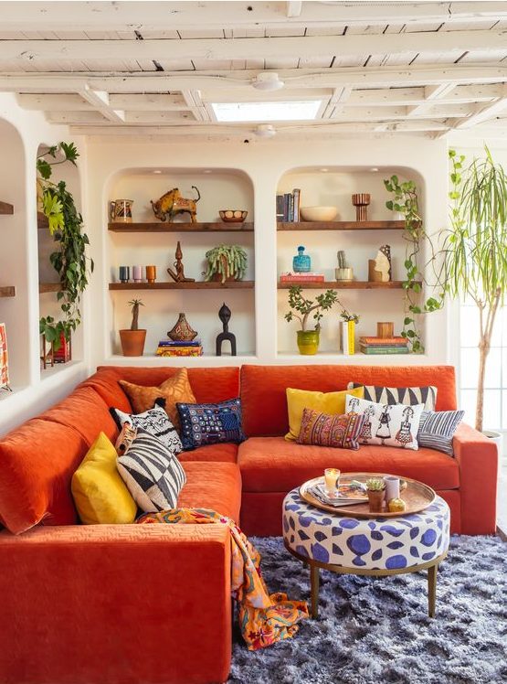 a vivacious living room with niches with built in shelves, an orange sofa, bold textiles and potted plants for a maximalist feel