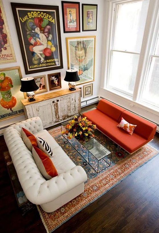 a whimsical living room with a bold gallery wall, a white tufted sofa, an orange sofa, a glass table and a shabby chic cabinet
