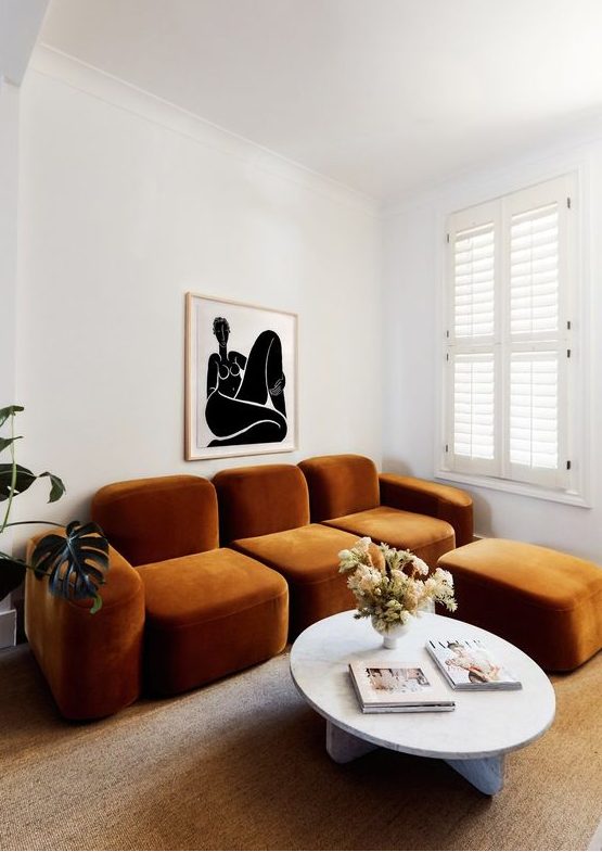 a whimsical living room with a quirky rust colored sofa and an ottoman, a round table and a bold artwork