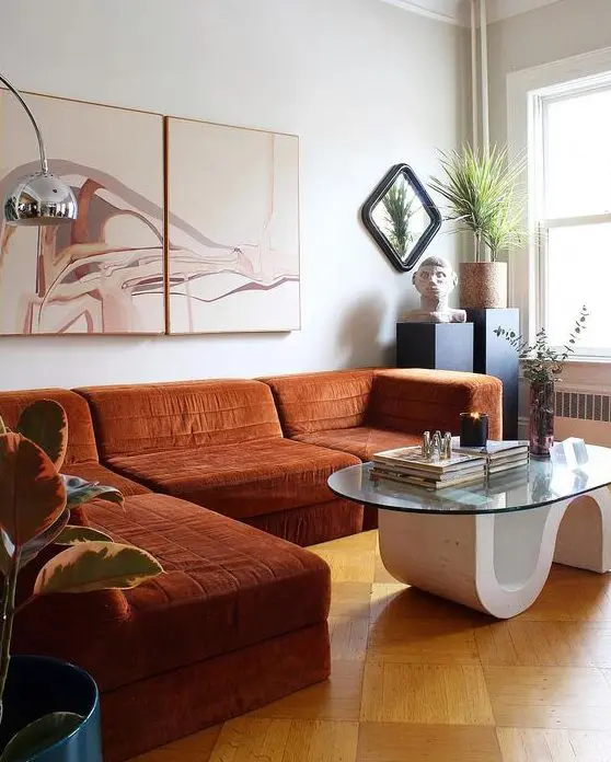 a whimsical space with a rust colroed sectional, a quirky table, potted plants and a lovely artwork is wow
