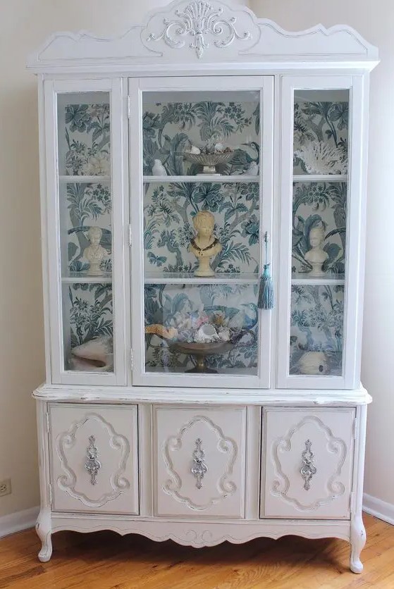 a white vintage cabinet with blue and white wallpaper inside for displaying souvenirs is a very sophisticated and beautiful idea