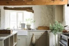 an English cottage kitchen with wooden beams, light green cabinets, rough walls and a large kitchen island