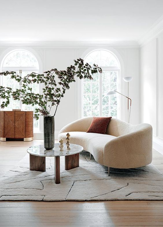 an airy Scandinavian living room with arched windows, a creamy curved sofa, a chic credenza and a three leg round table, a floor lamp