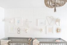 an airy twin nursery with an accent wall, grey crib, a wooden bead chandelier, neutral and printed bedding and a gallery wall
