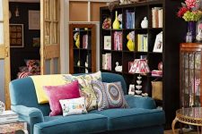 an eclectic living room with a blue sofa, a printed rug, colorful pillows, an ottoman with books, a dark-stained bookcase and bright decor