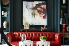 an elegant and moody living room with graphite grey walls, built-in storage units, a bold red leather sofa, white stools and elegant lamps and decor