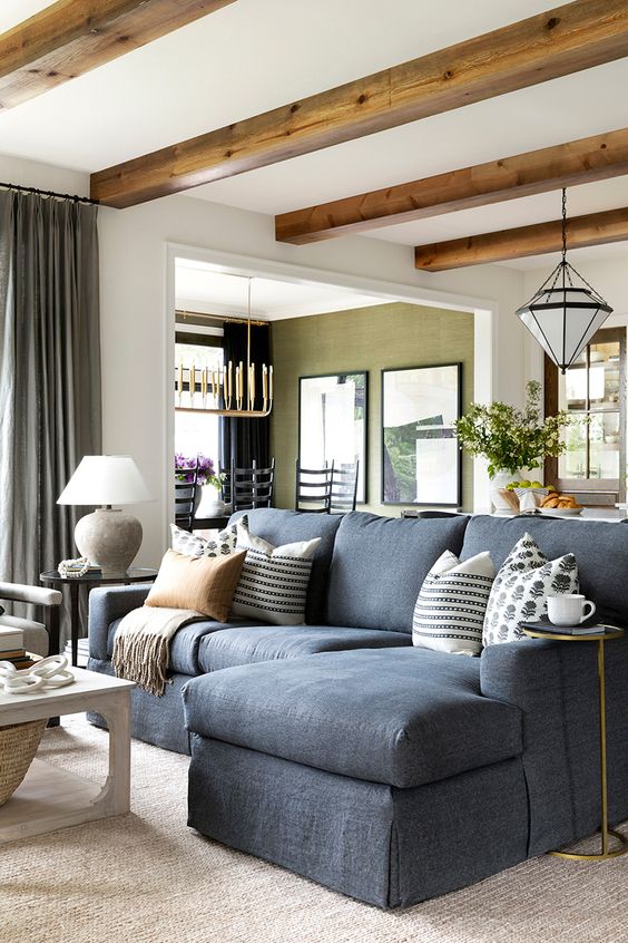 an elegant farmhouse living room with wooden beams on the ceiling a slate grey sofa neutral decor and a large rug