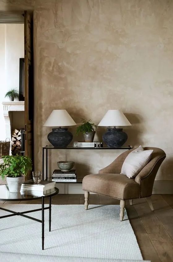 an elegant living room with beige limewashed walls, a glass console and coffee table, a brown chair and neutral textiles