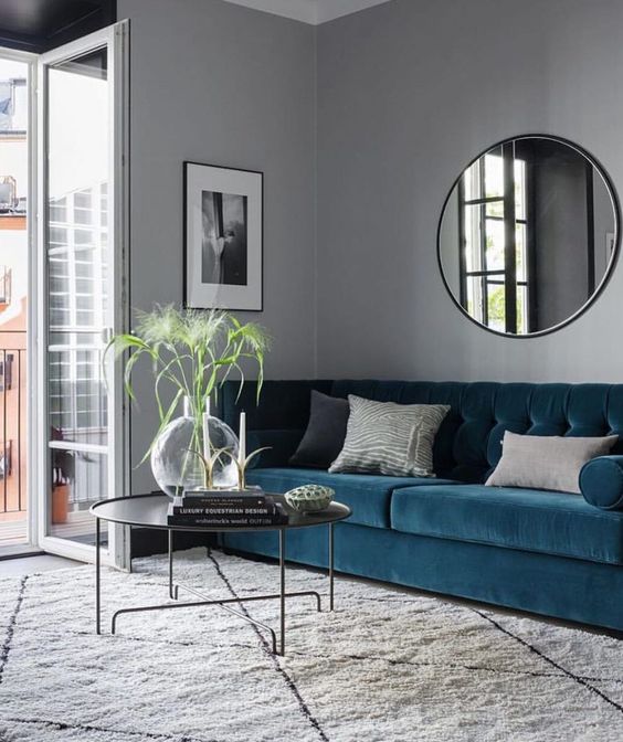 an elegant living room with grey walls, a blue sofa, a round coffee table, a round mirror and a black and white artwork