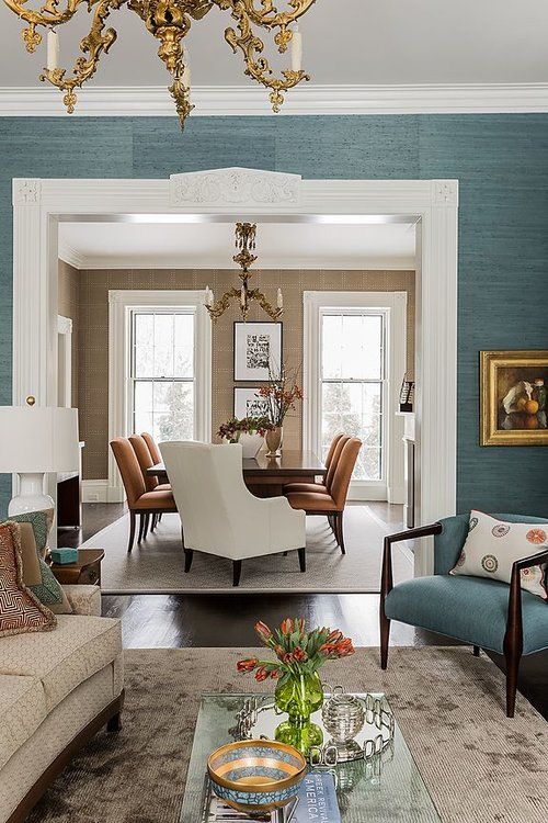 an elegant living room with turquoise grasscloth wallpaper, neutral and turquoise furniture, elegant gold chandeliers and chic artworks