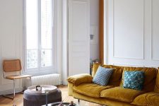 an exquisite Parisian living room with a mustard sofa, blush and brown chairs, a low glass table and a beautiful chandelier