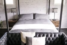 an industrial bedroom with a black leather tufted sofa at the foot of the bed that adds style