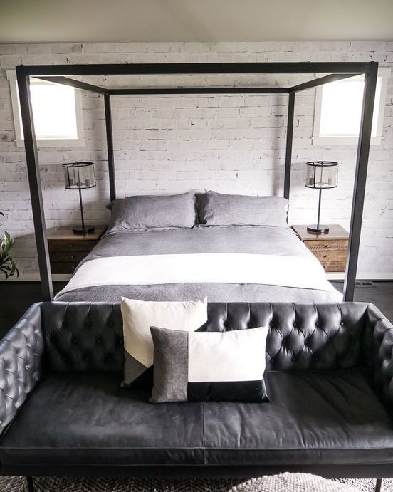 an industrial bedroom with a black leather tufted sofa at the foot of the bed that adds style