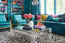 03 a bold and chic blue living room with bookcases, blue seating furniture, an acrylic table and a zebra print rug and touches of gold