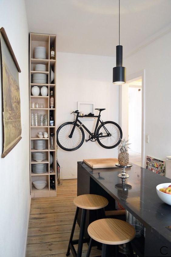 a chic contemporary dining and cooking space with an open storage shelf, a white rack for holding a bike, a black pendant lamp and a large kitchen island