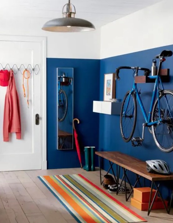 a colorful entryway with a bold blue wall, a holder for the bike, a bench and some hooks and hangers for various stuff is ultimate