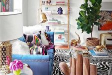 06 a maximalist living room with zebra printed rugs, a blue sofa with colorful pillows, a printed table, a glass shelving unit and a potted tree