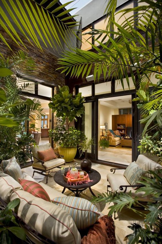 a small tropical inner backyard with black metal furniture and neutral upholstery, printed pillows, a metal table and lots of plants
