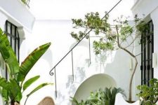 08 a small tropical patio with lots of potted plants, a white and wicker butterfly chair and all white walls around