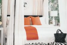 12 a stylish bedroom with green botanical print walls, a canopy bed with white curtains, orange and white pillows and zebra print stools at the foot of the bed