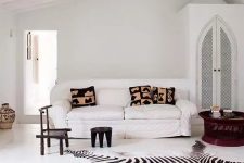 14 an eclectic white living room with a wardrobe, a white sofa, black stools, a mahogany coffee table and a zebra print rug plus printed pillows