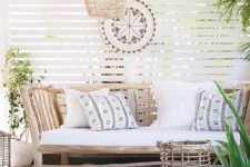 17 a welcoming tropical patio with a rustic wooden bench with pillows, a wicker lamp, a woven ottoman and a rattan candle holder