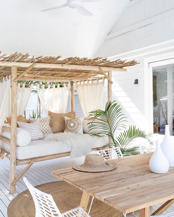 a welcoming tropical terrace with a wooden table, white metal chairs, a bench with a roof and lots of pillows