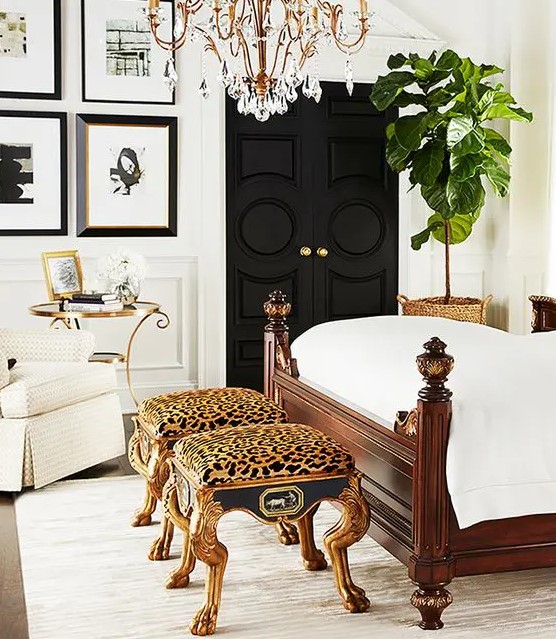 a gorgeous bedroom in neutrals, with black doors, a black and white gallery wall, a dark-stained bed with neutral bedding, a crystal chandelier and a couple of cheetah print stools