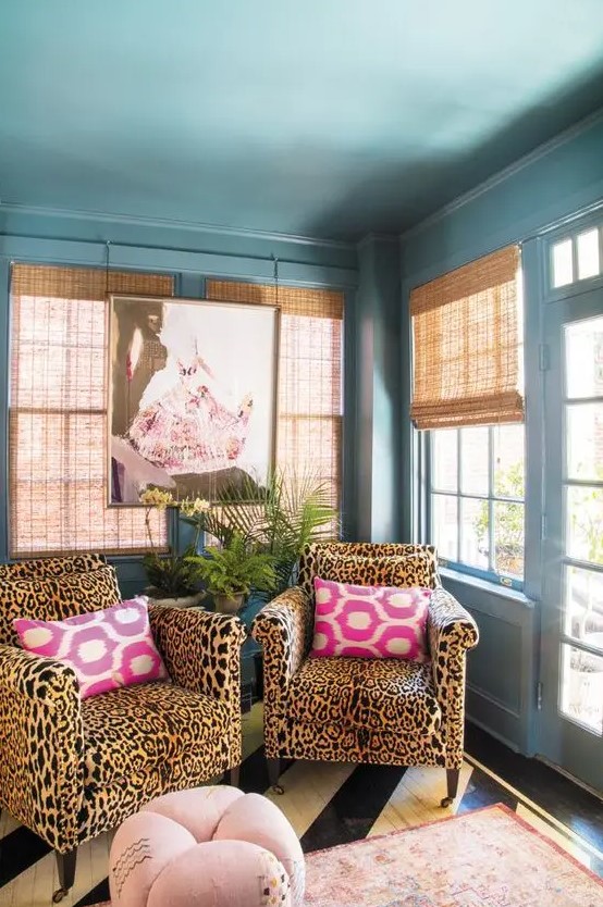 a maximalist space with a blue ceiling and walls, with cheetah print chairs, a pink rug and a pouf, potted greenery and woven shades