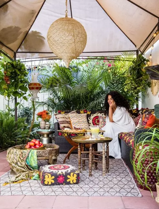 a bright boho tropical patio with a tent on top, boho textiles, colorful pillows and lots of potted plants around