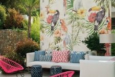 22 a colorful tropical patio with a white sofa and colorful pillows, hot pink chairs, a bright watercolor wall and little stools