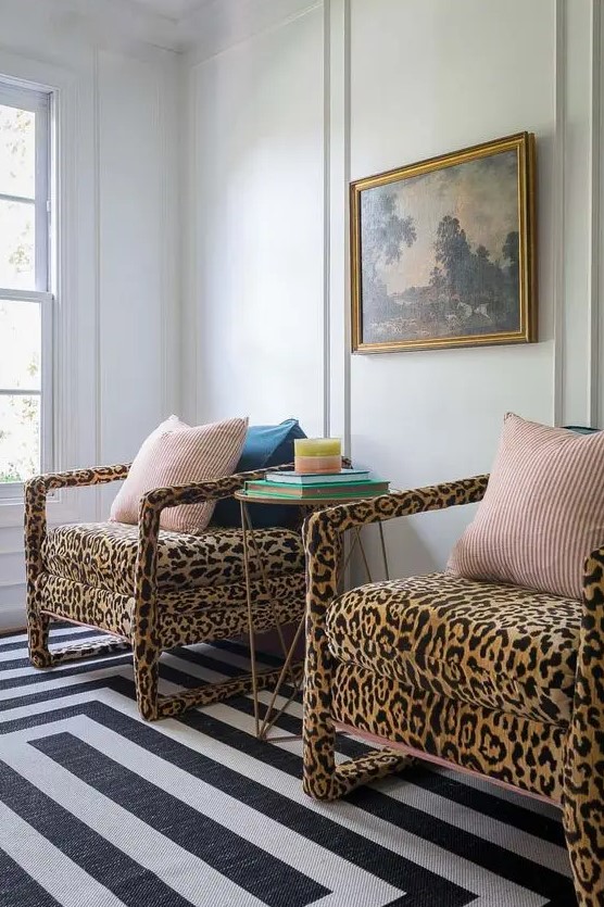 a stylish nook with a black and white striped rug, leopard print chairs, colorful pillows, a side table with books and a vintage artwork