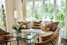 24 an exquisite living room done in neutrals, with a creamy sofa with printed pillows, leopard print chairs, layered rugs and a glass table