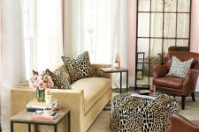 26 a pretty living room with pink walls, a tan sofa with leopard pillows and a leopard print pouf, a tan rug, a coffee table and a vintage framed mirror