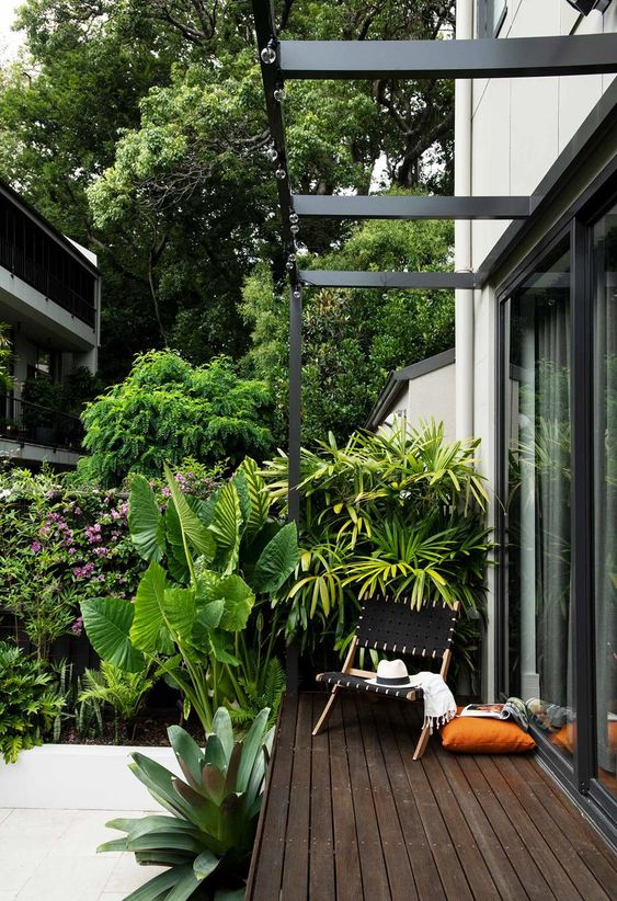 a small tropical deck with a black woven chair and some pillows, a super lush garden and a tiled floor next to the deck