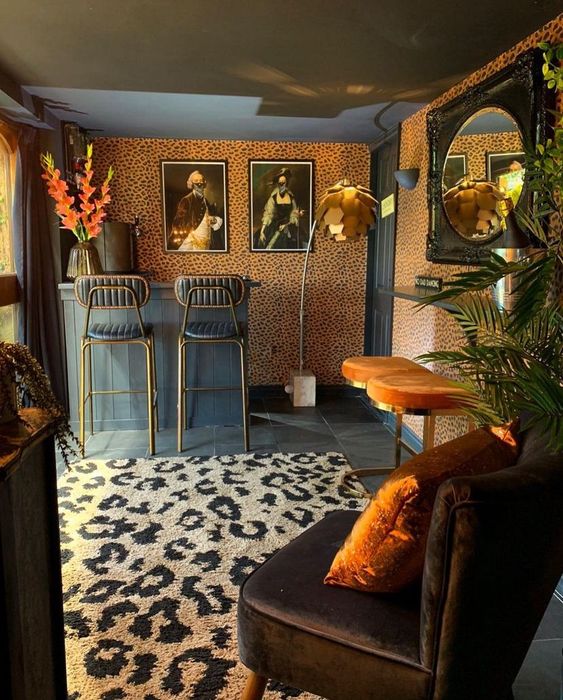 a bold space with a character, with cheetah print wallpaper and a rug, black and orange stools, a brown chair and vintage artwork on the wall