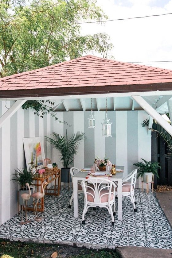 a tropical patio with a dining space done with white and pink rattan chairs, pink flamingos, a rattan bar table and potted plants