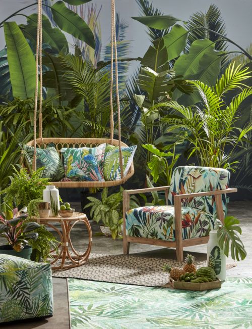a tropical terrace with wooden and rattan furniture, colorful upholstery and a rattan coffee table and layered rugs plus lots of tropical plants