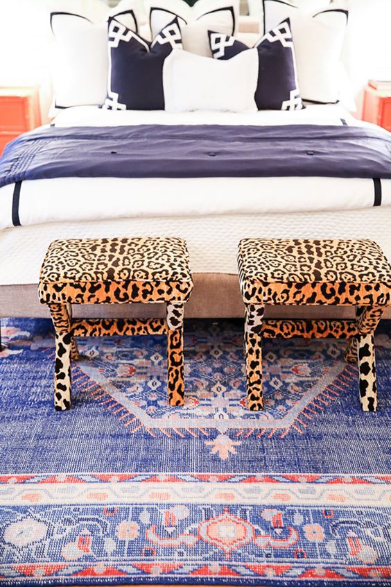 a beautiful blue bedroom with navy and white bedding, with a bright blue and red printed rug and cheetah stools for an accent