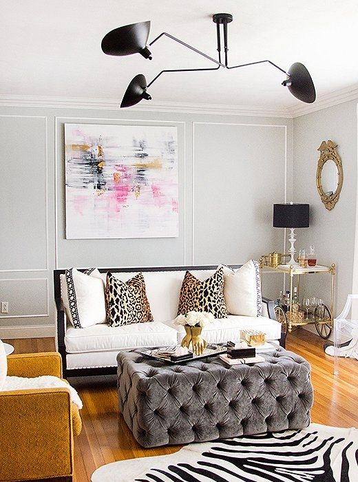 a glam midwest living room with grey walls, a white sofa with white and leopard print pillows, a grey pouf and a mustard chair plus a zebra print rug