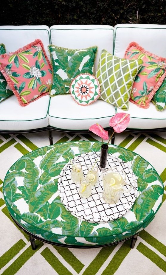 make up a boho patio with a large neutral sofa with colorful pillows and a tropical leaf print table