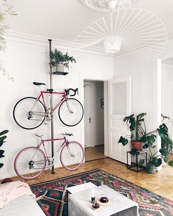 a serene and airy living room with a bright printed rug, potted greenery, a metal pillar with holders for bikes and a shelf with a plant