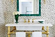 36 a stylish bathroom with Dolmatin print walls, a free-standing sink on gold legs, a mirror in a green frame and gold sconces is wow