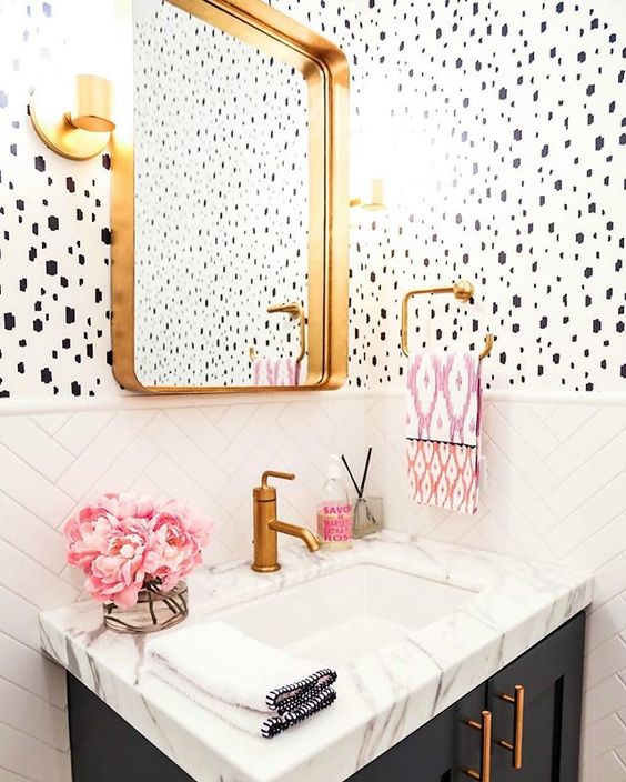 an elegant and chic powder room with Dolmatin print wallpaper, white chevron tiles, a navy vanity with a white sink, a gold framed mirror