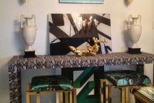42 an elegant nook with a snakeskin print console table, emerald and gold stools, a black and white artwork, white vases and gold sconces