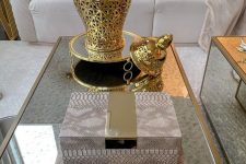 44 a glam space with a glass coffee table, pink snakeskin print boxes, a gold vase on a gold stand and white blooms