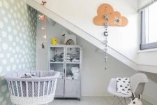 a Nordic attic nursery with a printed wall, a grey storage cabinet, a grey crib on casters, a grey chair and a rug plus toys