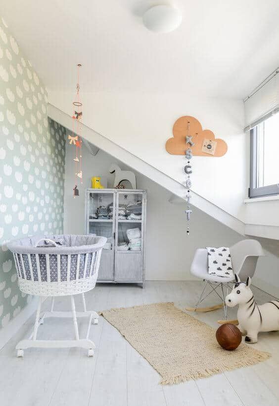 a Nordic attic nursery with a printed wall, a grey storage cabinet, a grey crib on casters, a grey chair and a rug plus toys