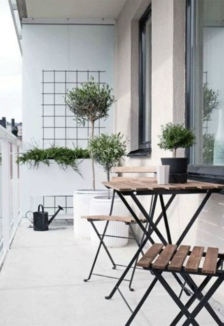 a Nordic balcony in black and white, with a planter and some greenery and trees, wooden folding furniture, a black watering can