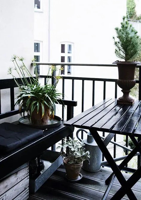 a Nordic balcony in black, with simple wooden furniture, potted greenery and blooms is a stylish idea for those who love moody colors